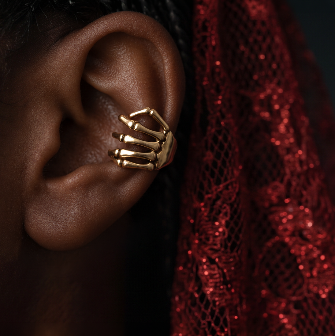 Golden Skeleton Hand ear cuff worn on the ear against deep red sparkly lace
