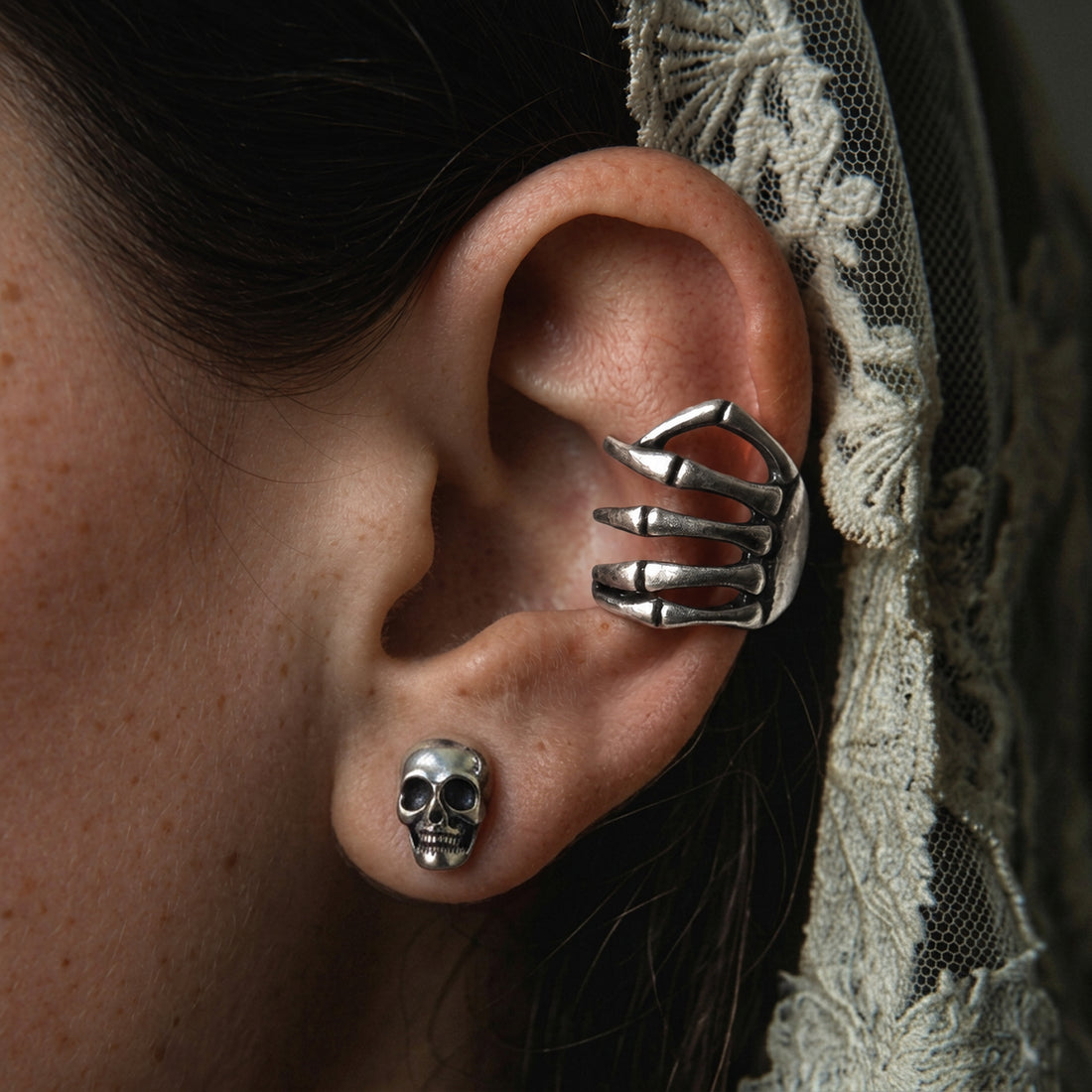 Silver Skeleton Hand ear cuff worn on the ear above a small silver skull stud, cream lace veil behind