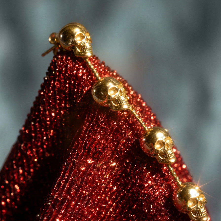 Skull Chain Drop earrings, gold skulls on a beaded line against sparkly red fabric