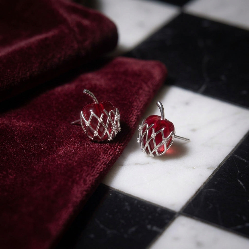 Bravo Apple stud earrings pair on a black and white checkered floor beside red velvet, red apples in a silver lattice