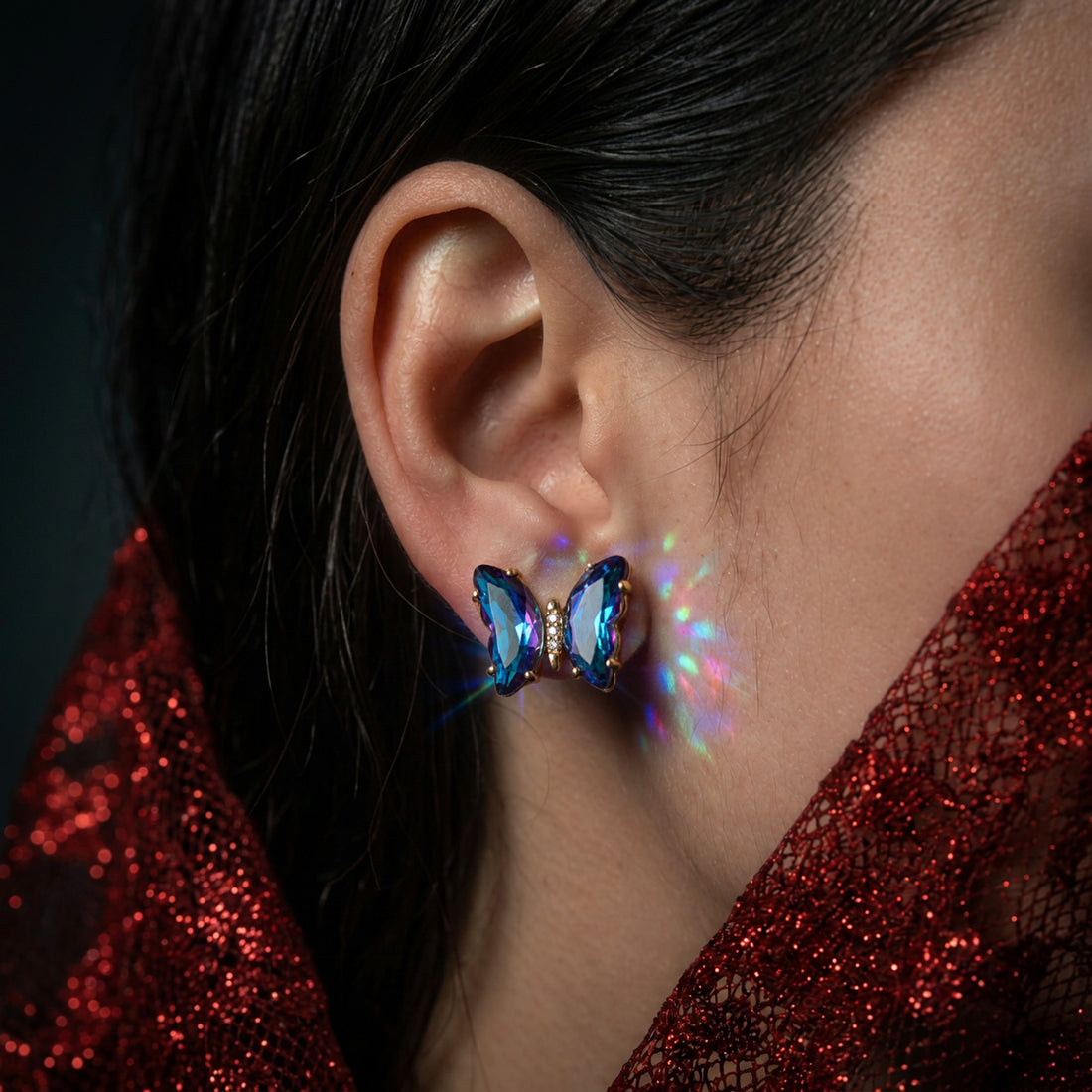 Nebula Crystal Butterfly earring worn on the ear, blue crystal wings, with a red glitter mesh collar