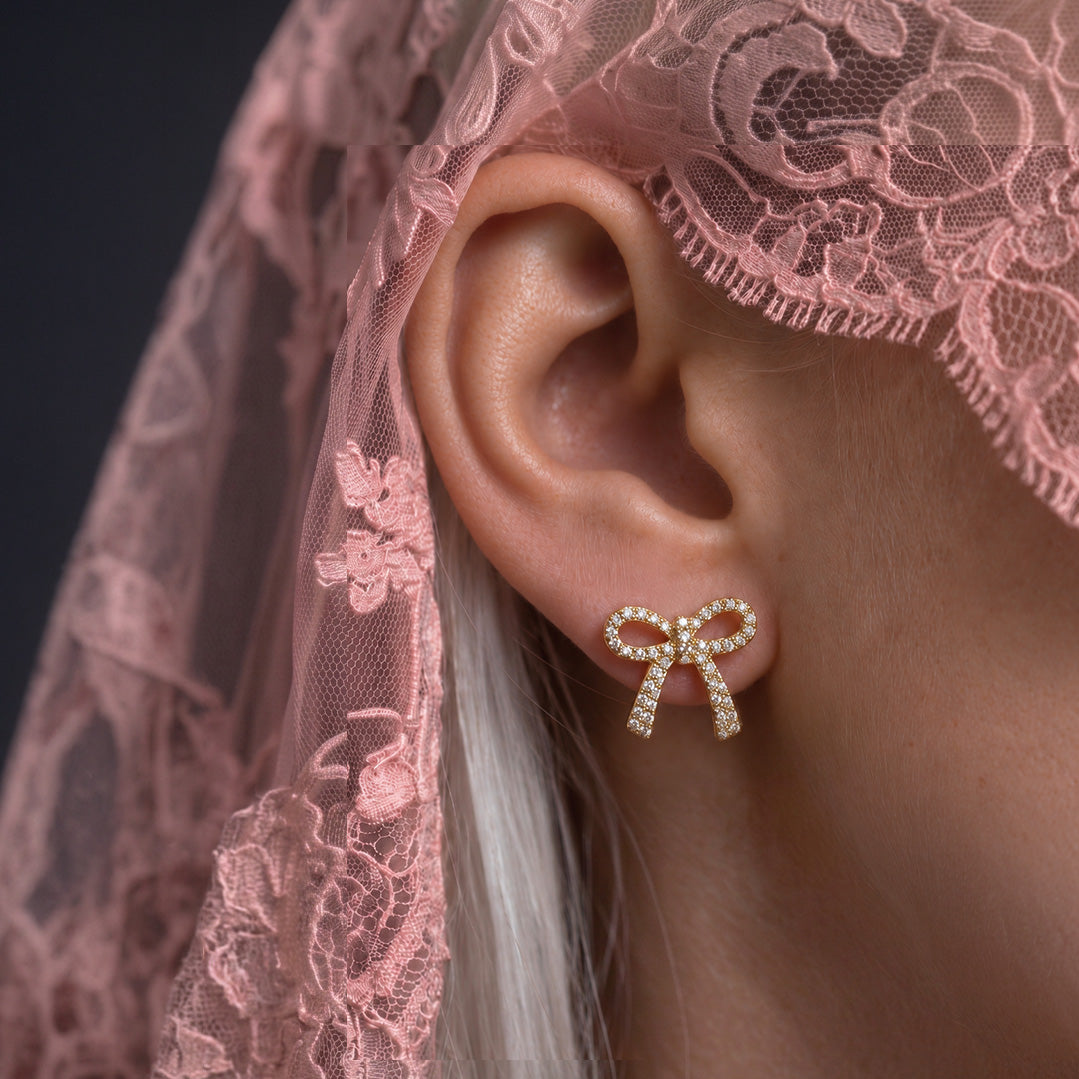 Crystal Bow stud earring worn on the ear, crystal-set gold bow, with a pink lace veil and white hair
