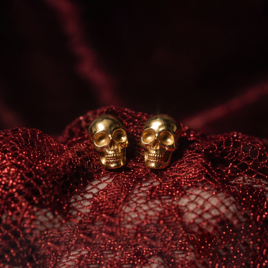 Gold Skull stud earrings, a pair of gold skulls resting on red glittery mesh fabric