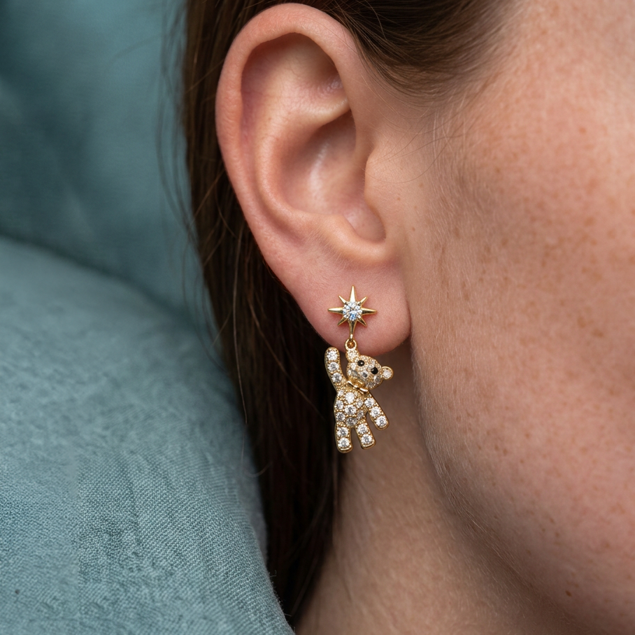Teddy Bear crystal drop earrings worn on the ear, gold bear hanging from a star stud, teal cushion behind
