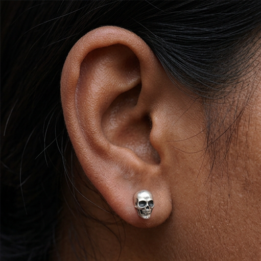 Silver Skull stud earrings, a small silver skull stud worn on the ear, shown against dark hair