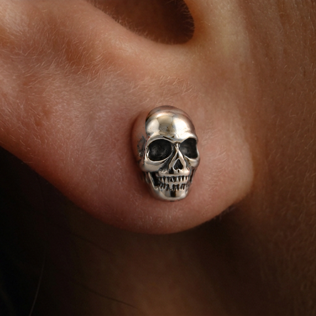Silver Skull stud earrings close-up, a detailed silver skull with teeth and dark eye sockets worn on the ear