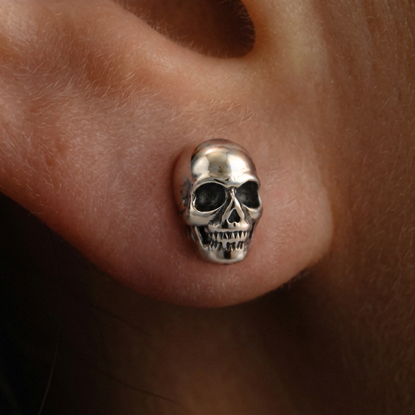 Silver Skull stud earrings close-up, a detailed silver skull with teeth and dark eye sockets worn on the ear