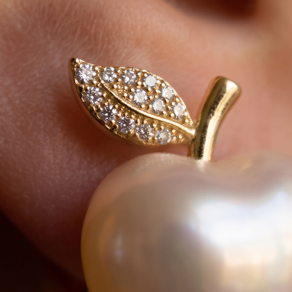 Pearly Apple earrings, macro of a crystal-set gold leaf and stem above a white pearl apple