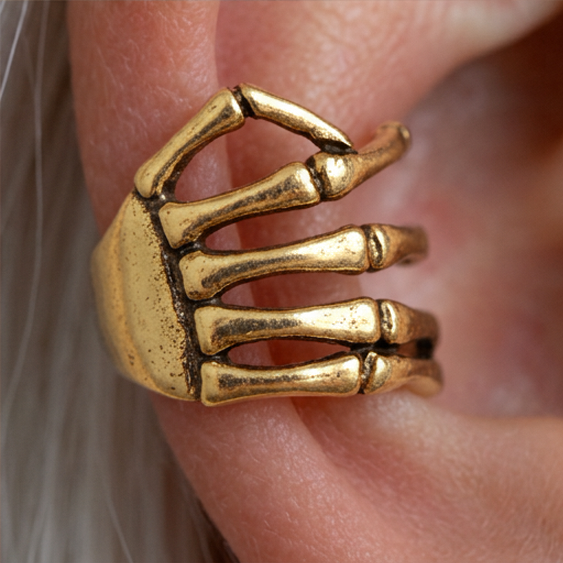Golden Skeleton Hand ear cuff worn on the ear, close-up of the gold bony fingers and palm