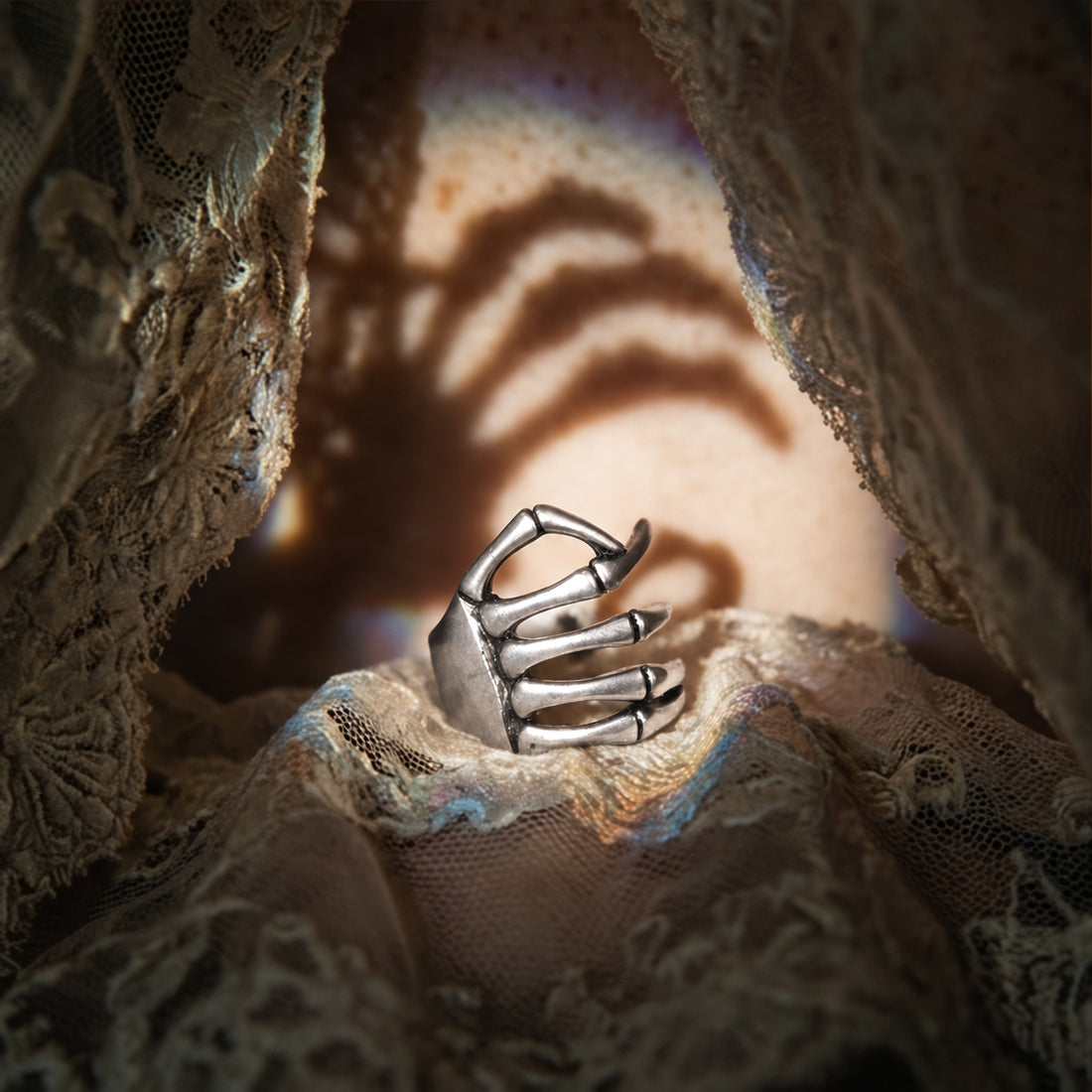 Silver Skeleton Hand ear cuff standing in draped lace, skeleton fingers with a hand shadow on the wall behind