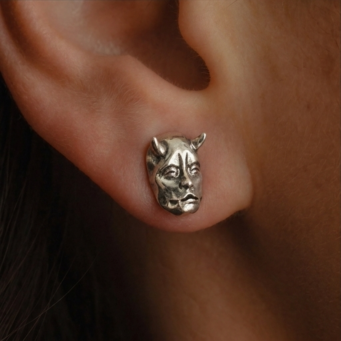 Jekyll & Hyde stud earrings, close-up of a silver horned face worn on the ear
