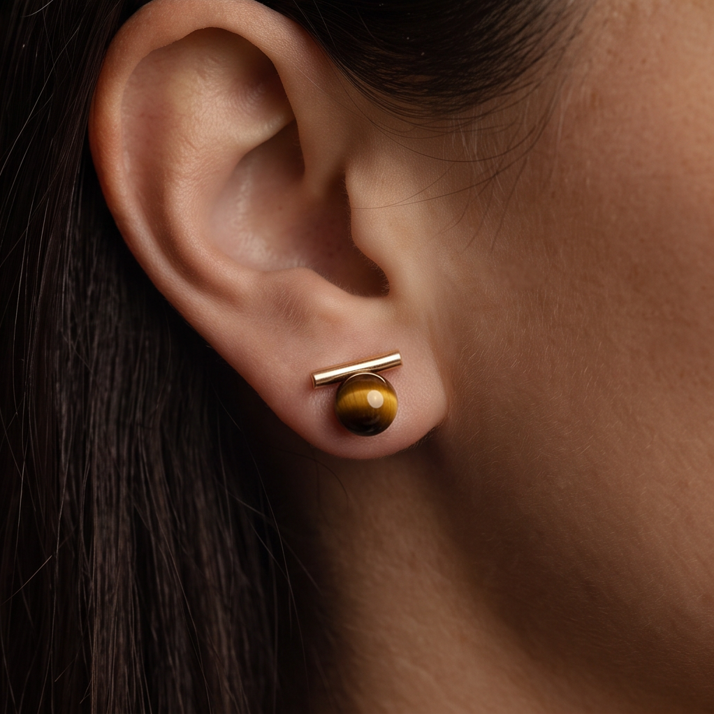 Wood Orb Bar stud earrings, a gold bar over a round brown bead worn on the ear, dark hair