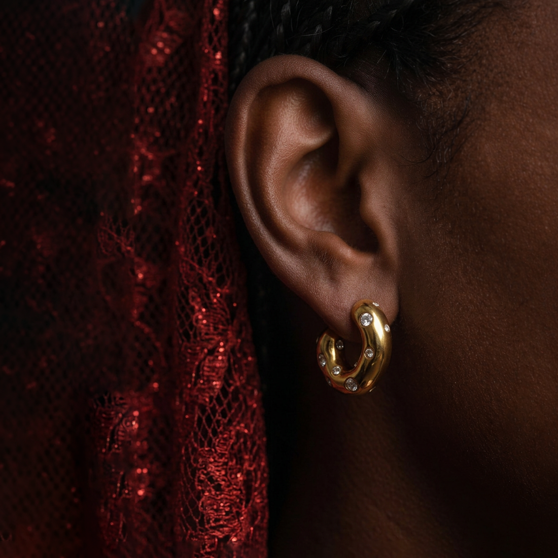 Chunky Spot crystal hoop earrings worn on the ear against dark red glitter lace