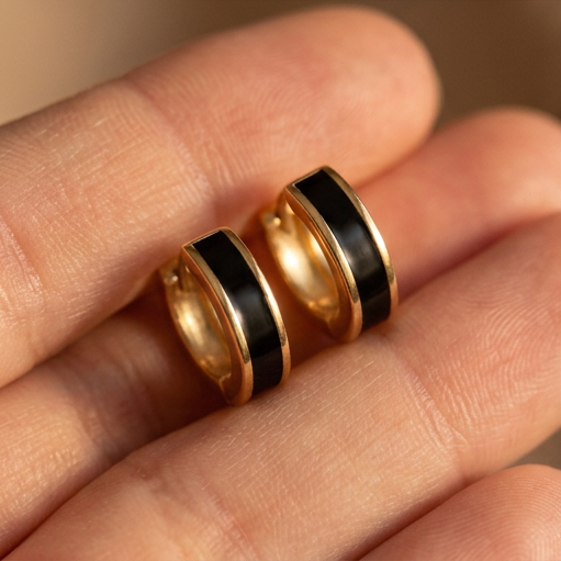 Caviar small hoop earrings held in a hand, two gold hoops with black center bands between fingers