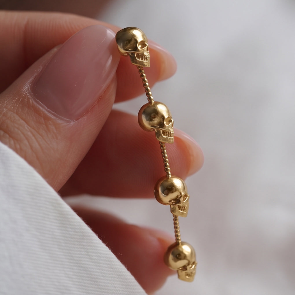 Skull Chain Drop earring close-up held between fingers, four gold skulls linked by tiny beads