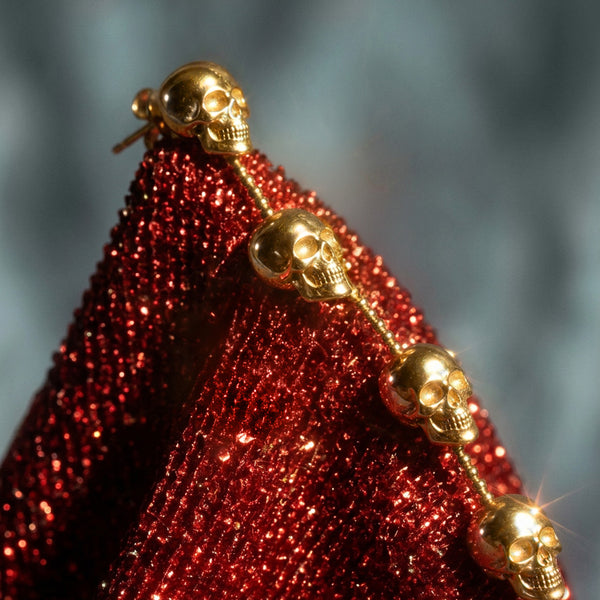 Skull Chain Drop earrings, gold skulls on a beaded line against sparkly red fabric