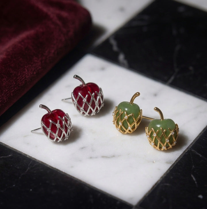 Granny Smith Apple stud earrings in green with gold lattice beside a red pair, on white and black marble