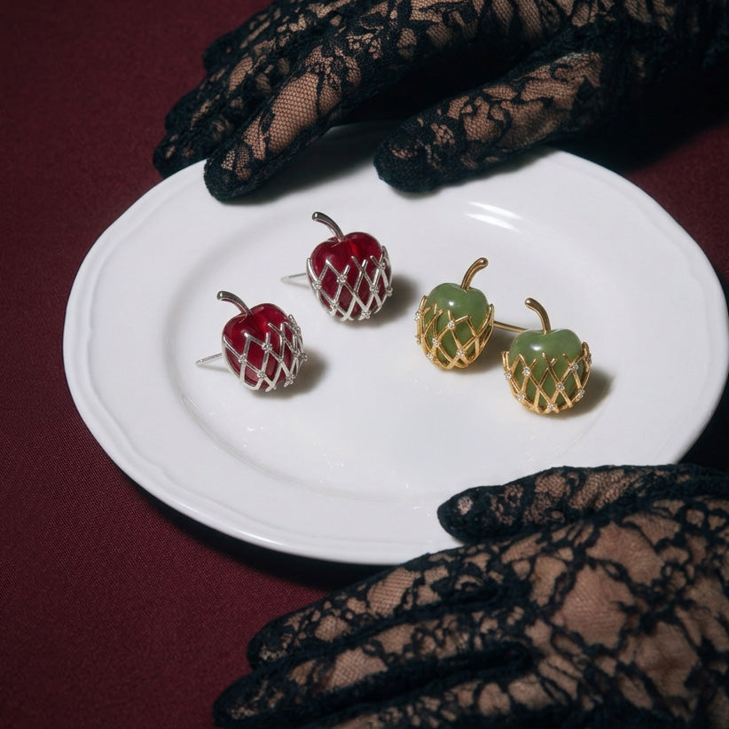 Bravo Apple stud earrings on a white plate, red apples in silver lattice and green apples in gold, black lace gloves