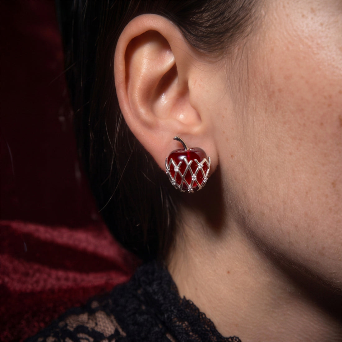 Bravo Apple stud earring worn on the ear, red apple in a silver lattice, with black lace at the neckline