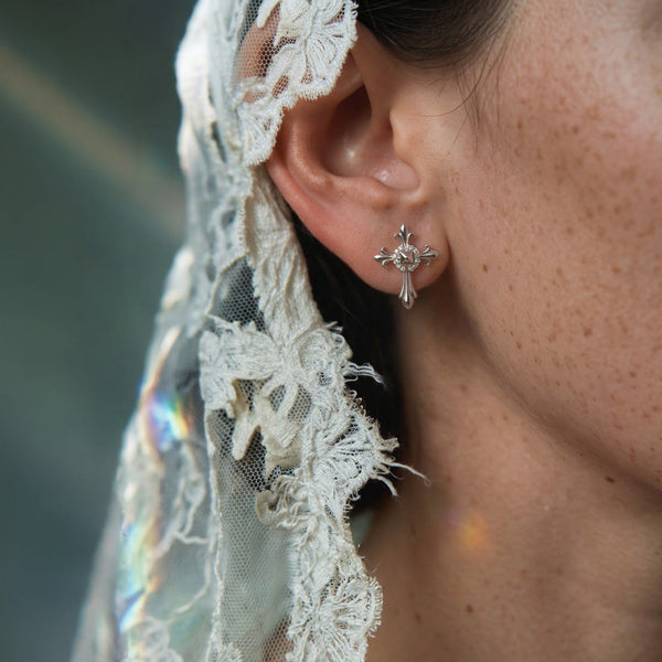 Melrose Cross crystal earring worn on the ear, small silver cross against a cream lace veil