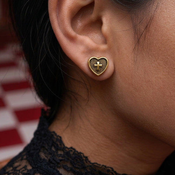 Heart cross stud earrings worn on the ear, a gold heart with a cross, against a black lace collar