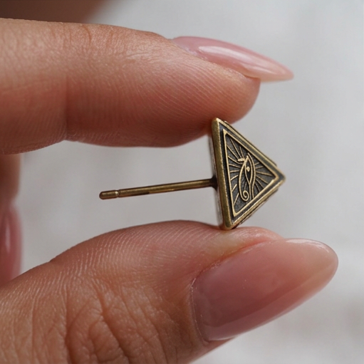 Pyramid stud earrings, a single gold triangle-shaped stud with an eye engraving held between fingers