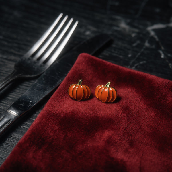 Pumpkin Patch stud earrings pair on a red velvet cloth beside a fork and knife on a dark marble table