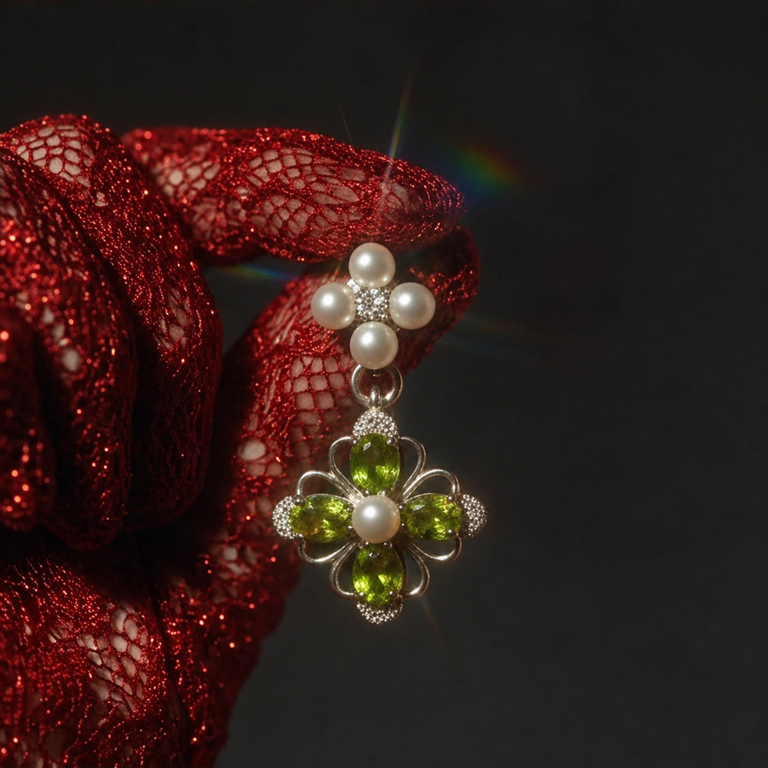 Victorian Crystal Drop earring held in a hand wearing a red glitter mesh glove, green jewels and pearls