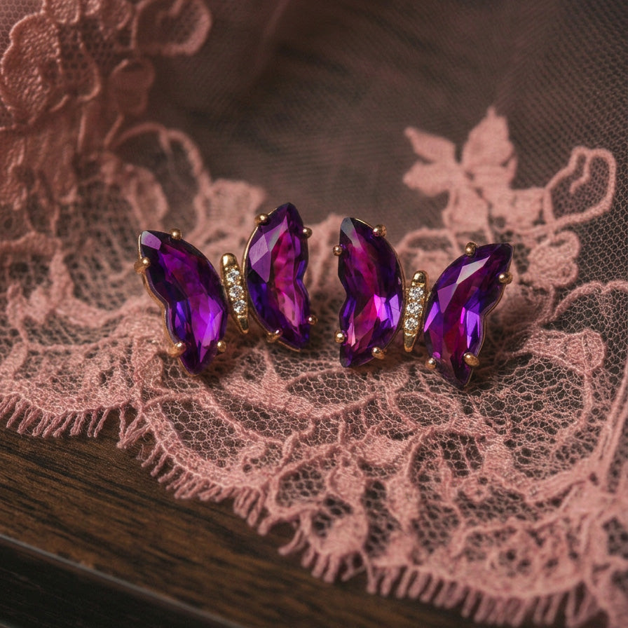 Aurora Crystal Butterfly earrings pair on pink lace, purple crystal wings on a dark wood surface