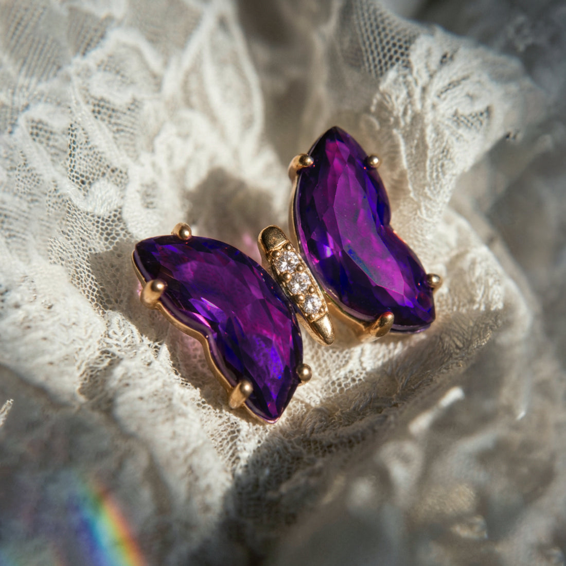 Aurora Crystal Butterfly earrings close-up on cream lace, purple crystal wings with a small crystal-set body