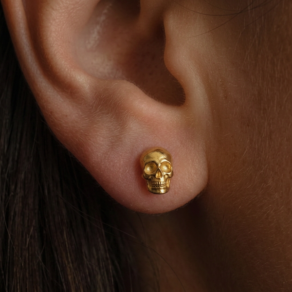 Gold Skull stud earrings, a small gold skull stud worn on the ear, shown against dark hair