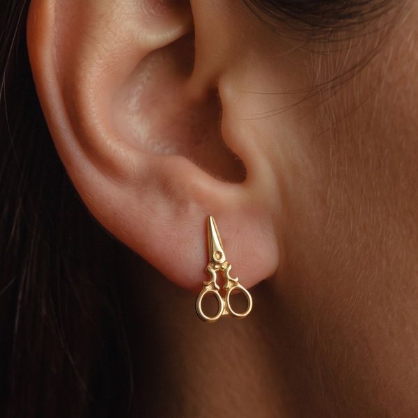 Scissors stud earrings worn on the ear, a small gold scissors with open loop handles, close-up