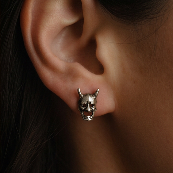 Devil Mask stud earrings; a silver horned mask with an open mouth worn on the ear