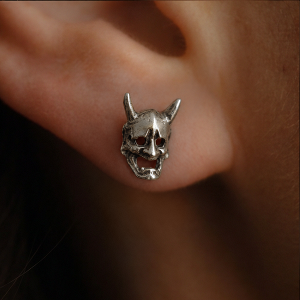 Devil Mask stud earrings; close-up of a silver horned mask worn on the ear