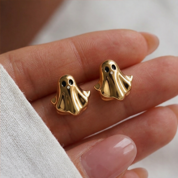 Golden Boo stud earrings, two gold ghosts with black eyes held in a hand beside a white knit sleeve
