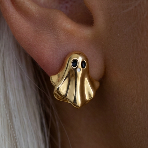 Golden Boo stud earrings, a gold ghost with black eyes worn on the ear, close-up with white hair
