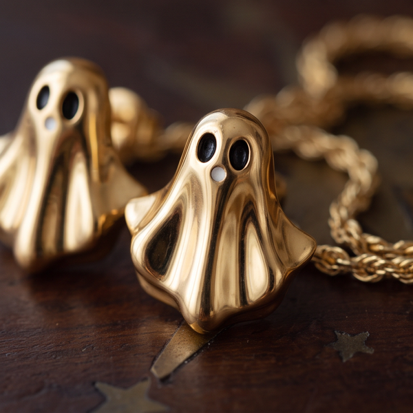 Golden Boo stud earrings, two gold ghosts on a dark wooden surface beside gold rope jewelry