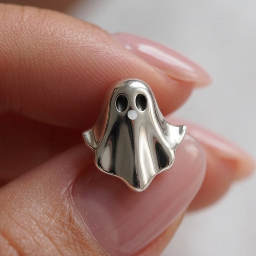 Silver Boo stud earrings, a silver ghost with black eyes held between fingertips, close-up