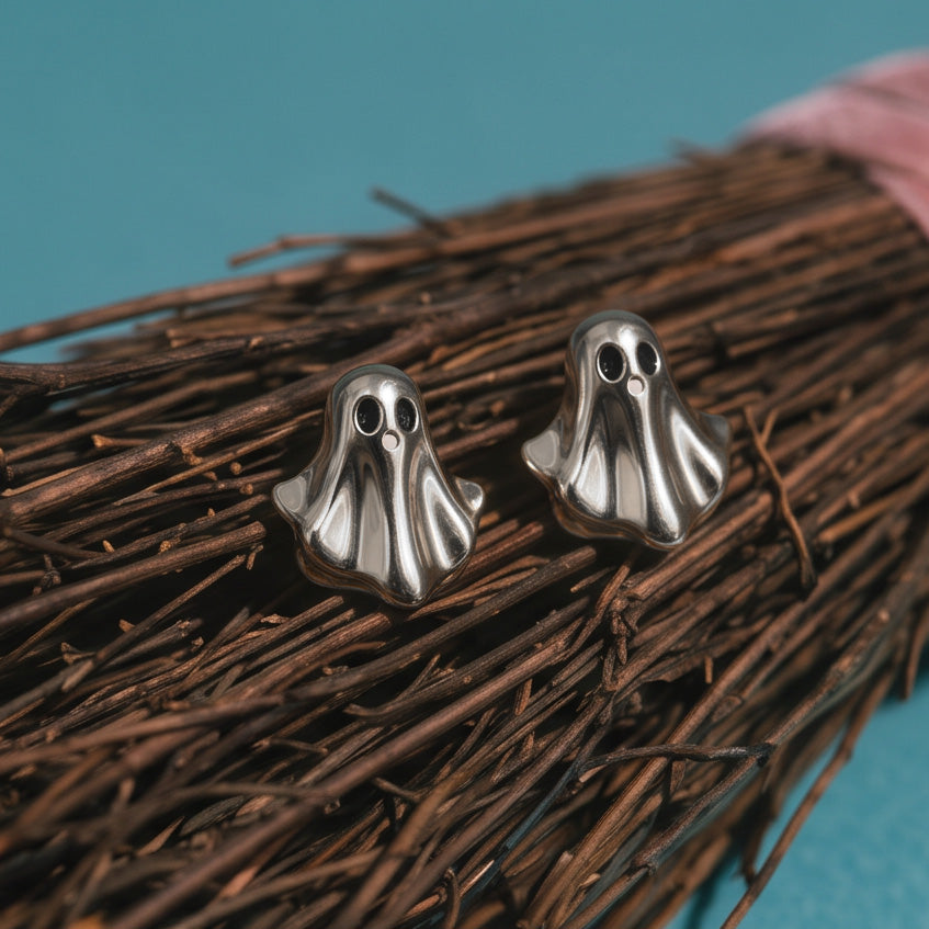 Silver Boo stud earrings, two silver ghosts resting on a twiggy broom with a teal background