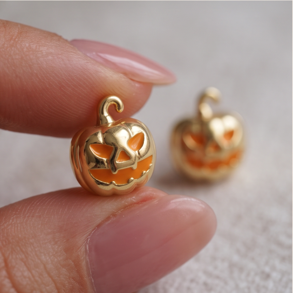 Golden Jack Pumpkin stud earrings held between fingertips, a gold pumpkin with an orange carved face