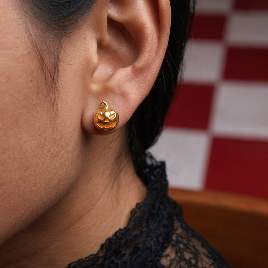 Golden Jack Pumpkin stud earrings worn on the ear, a gold jack-o'-lantern with orange face, black lace collar