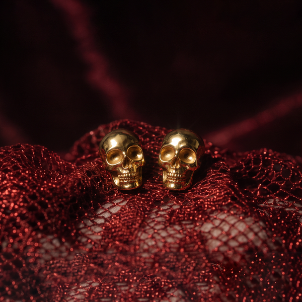 Gold Skull stud earrings, a pair of gold skulls resting on red glittery mesh fabric