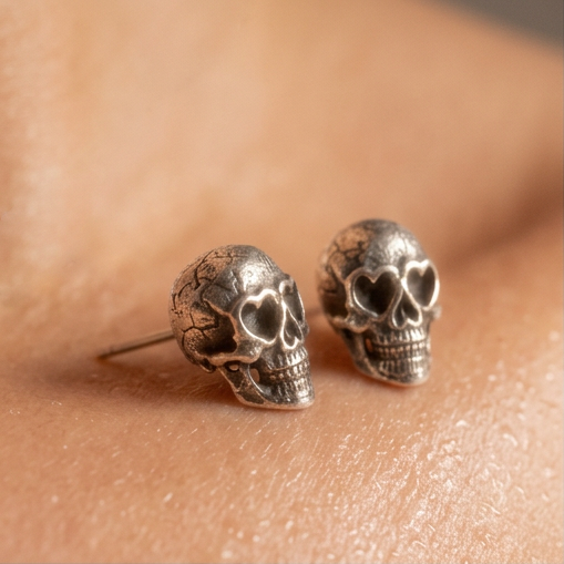 Lovestruck Skull stud earrings with heart-shaped eyes resting on bare skin, close-up