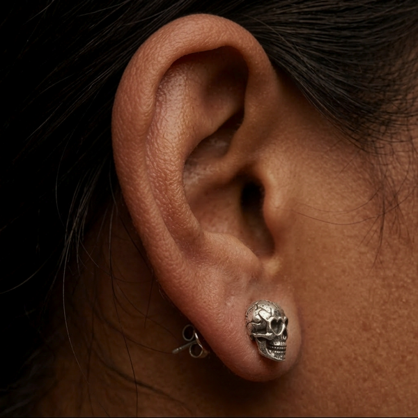 Lovestruck Skull stud earrings, a single silver skull with heart eyes worn on the ear, close-up