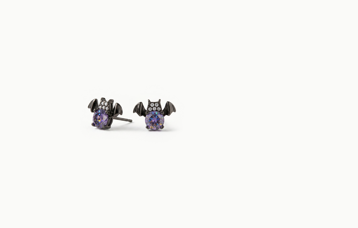Black bat stud earrings holding a purple crystal