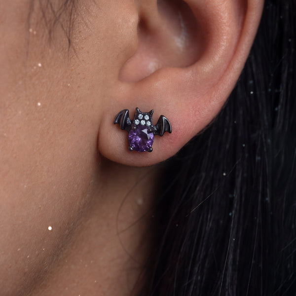 Nightshade Crystal Bat stud earrings worn on the ear, a dark bat with a purple crystal body and small white crystals