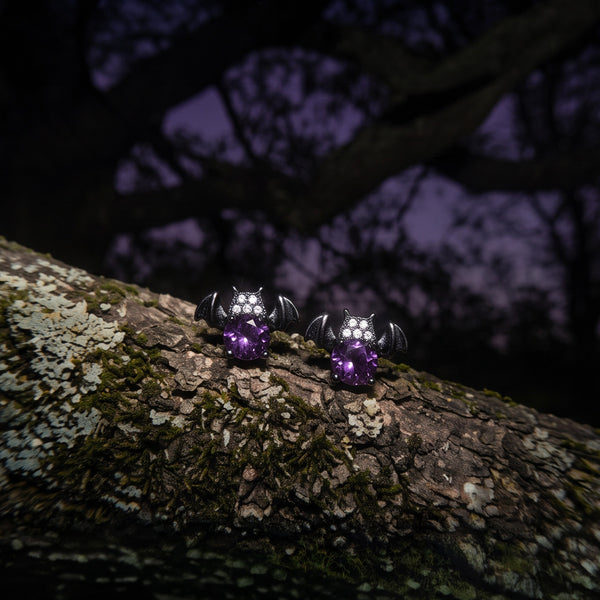 Nightshade Crystal Bat stud earrings, two dark bats with purple crystals on a mossy branch at dusk