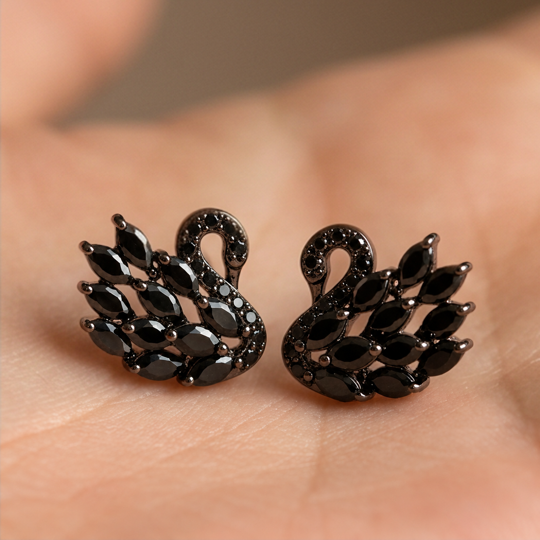 Black Swan earrings held in an open palm, a pair of black crystal swans facing each other