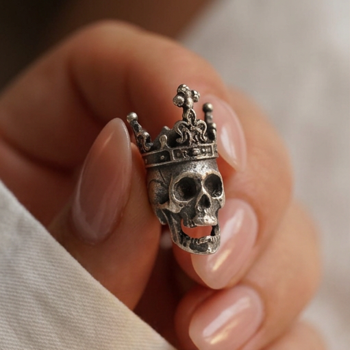 Skull King stud earrings, a crowned silver skull held in a hand against a white linen sleeve