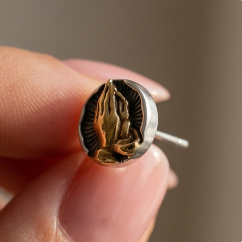 6ix Hands stud earrings pinched between fingertips, gold praying hands on a silver coin